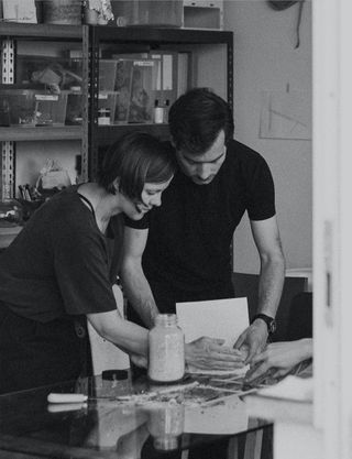 A black and white portrait of designers Archibald Godts and Theresa Bastek of Studio Plastique, working in their studio