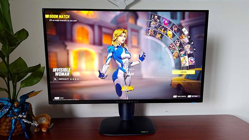 Alienware AW2725Q gaming monitor sitting on woodgrain desk next to plant with Marvel Rivals on screen and Invisible Woman selected on character screen.