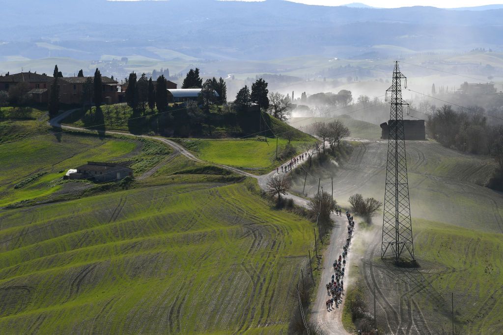 SIENA ITALY MARCH 06 The Peloton passing through a gravel strokes sector during the Eroica 15th Strade Bianche 2021 Mens Elite a 184km race from Siena to Siena Piazza del Campo Dust Landscape Tuscany StradeBianche on March 06 2021 in Siena Italy Photo by Tim de WaeleGetty Images