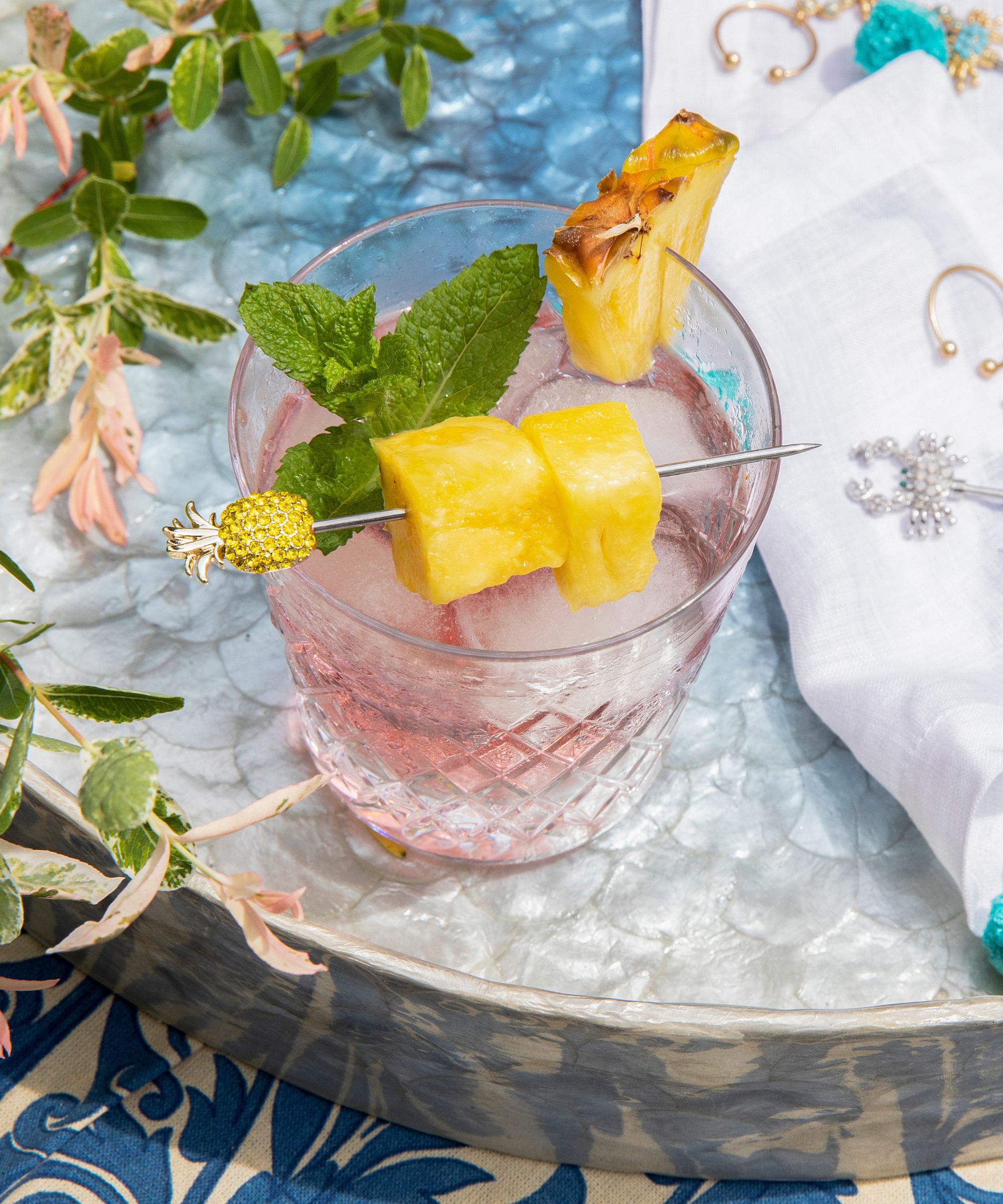 Cocktail glass with pineapple garnish on a pineapple pick with foliage around it