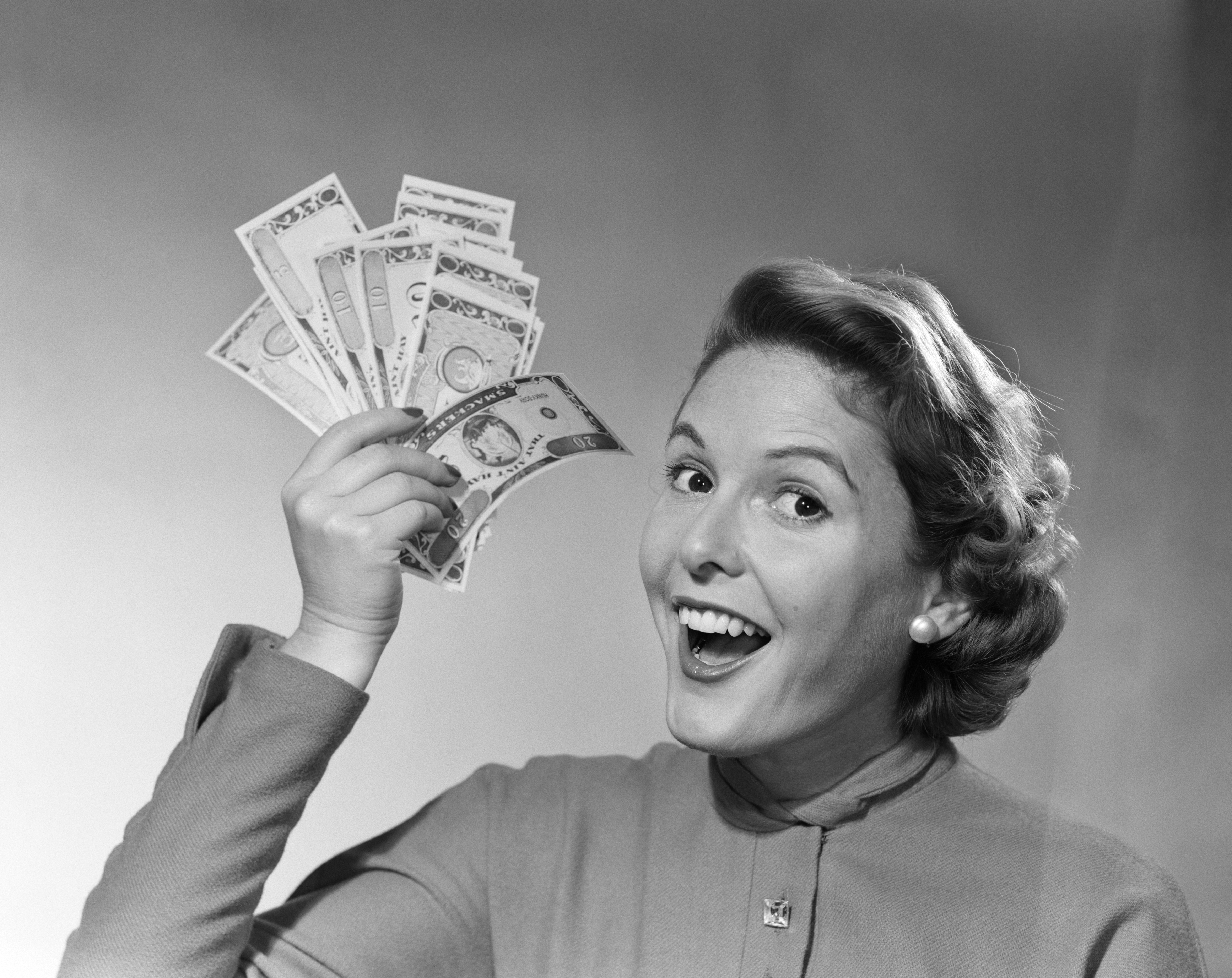 A black and white photograph of a woman holding up a handful of money