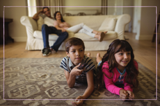 two children watching TV on the floor with parents in background