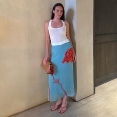 a woman wearing a white tank top, blue skirt, and red sandals