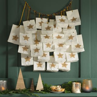 Bags decorated with stars on a circle above Christmas decorations, mince pies and candles on a grey panelled wall
