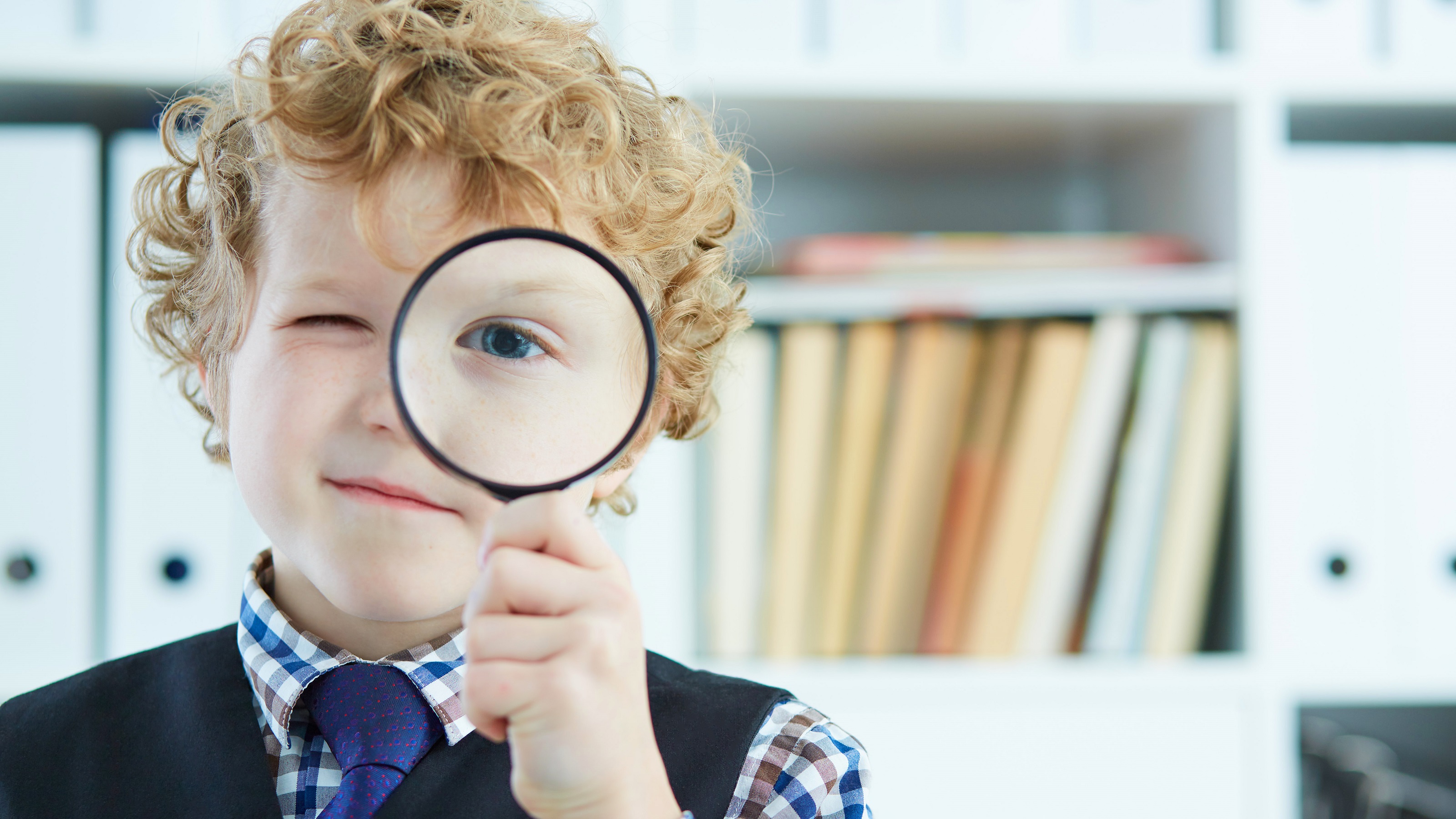 A young boy holds a magnifying glass up to his eye.