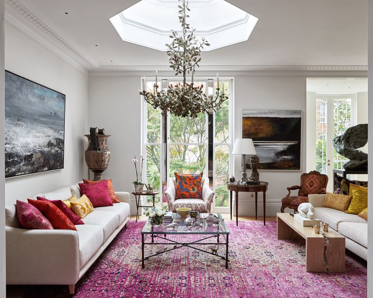 Living room with a large chandelier hanging from the skylight with pink carpet below