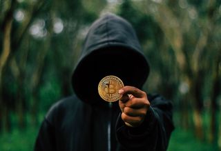 A hooded figure holding a fake bitcoin