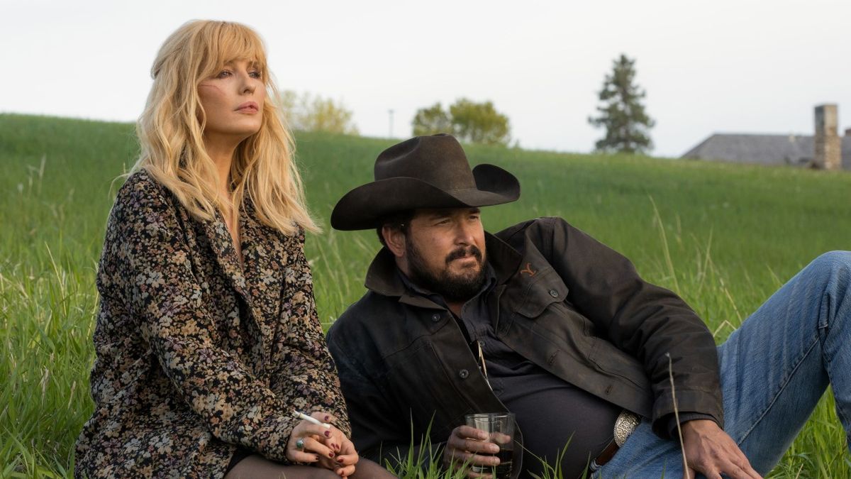 Beth and Rip sitting in the grass during party on Yellowstone