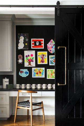 closet home office with sliding door, desk, wooden chair, kids artwork on wall, white units