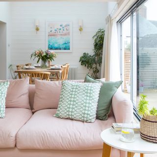 Living/dining room area with a pink sofa and green curtains, a dining table behind it, and white curtains hanging above the sliding doors