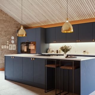 blue kitchen with island and bar stools with wood ceiling and gold pendant lights