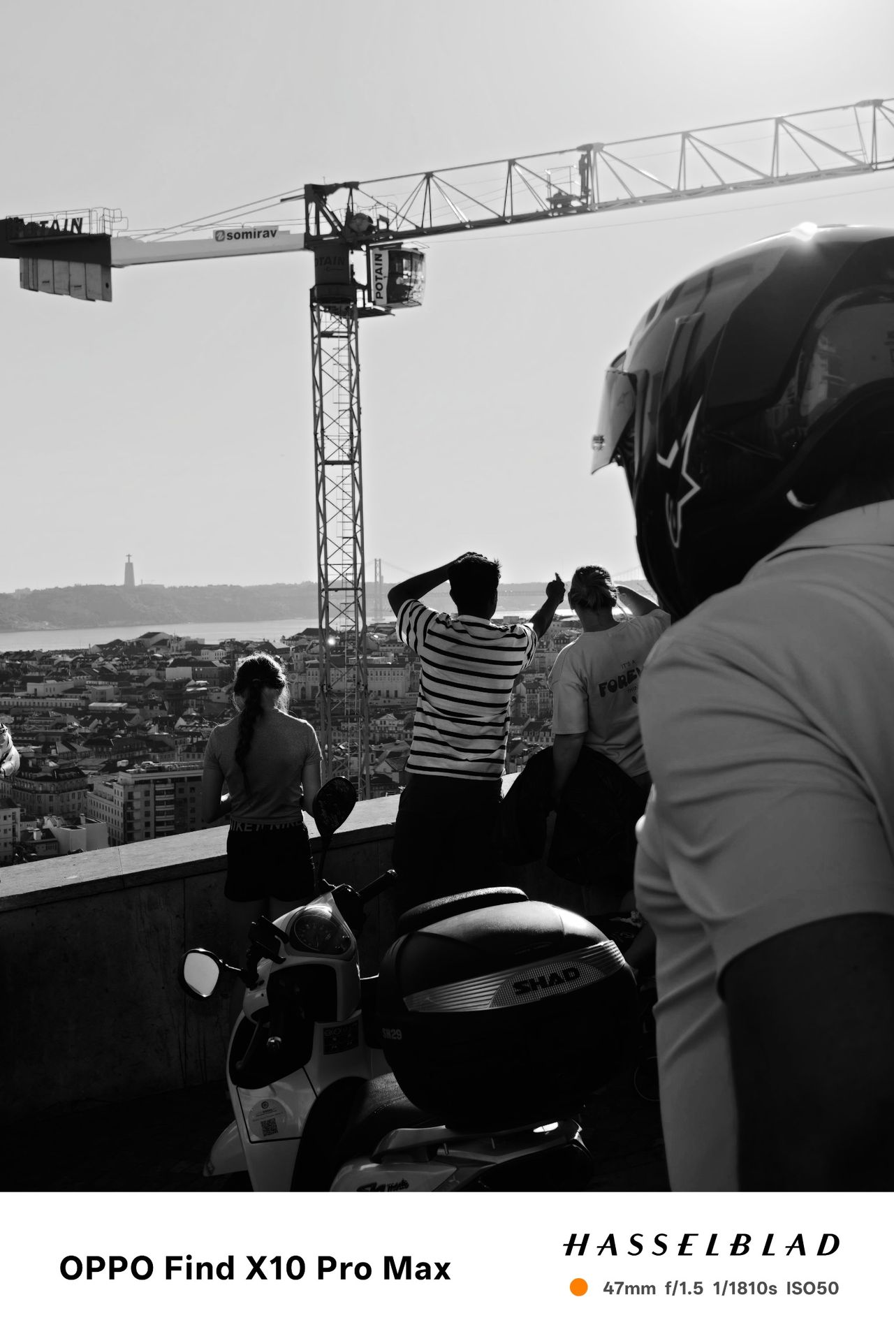 Black-and-white view over Lisbon with people, a scooter and a construction crane in the foreground.