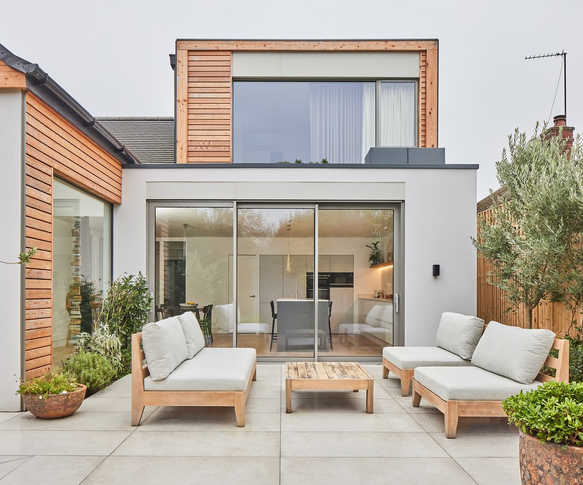 The exterior of a house with a light stoned patio and outdoor sofas