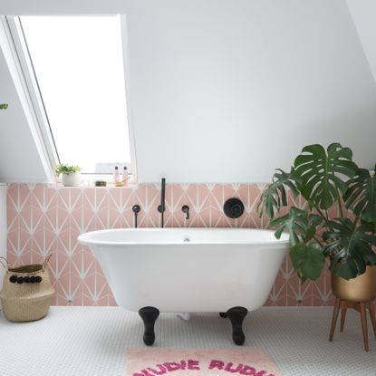 White bathroom with sloped ceiling and pink geometric tiles, with a small freestanding bath on a floor tiles with white mosaics