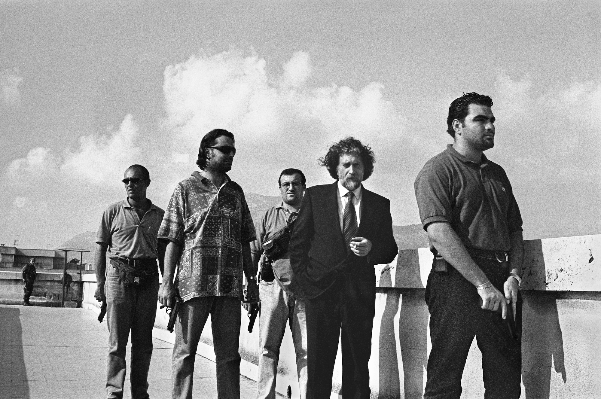 Black and white photograph of a man in a suit accompanied by four armed men