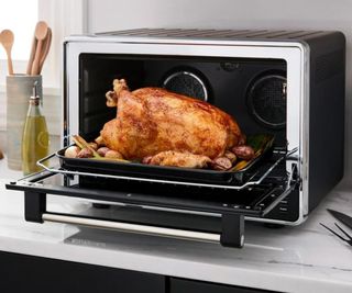 A chicken roasting in a KitchenAid Countertop Convection Oven with Air Fryer on a kitchen counter.