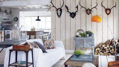 living room in a cabin with antlers on wall, white wood wall panelling and simple, rustic furniture