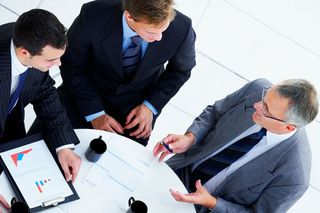 Three men in suits in conversation around a table