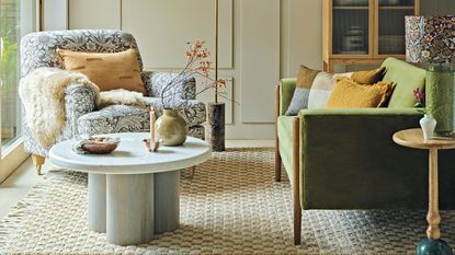 Neutral living room with green velvet sofa and an armchair upholstered in a neutral William Morris pattern next to a marble coffee table