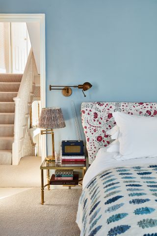 Blue walls and floral bedhead in Victorian home with view of stairs