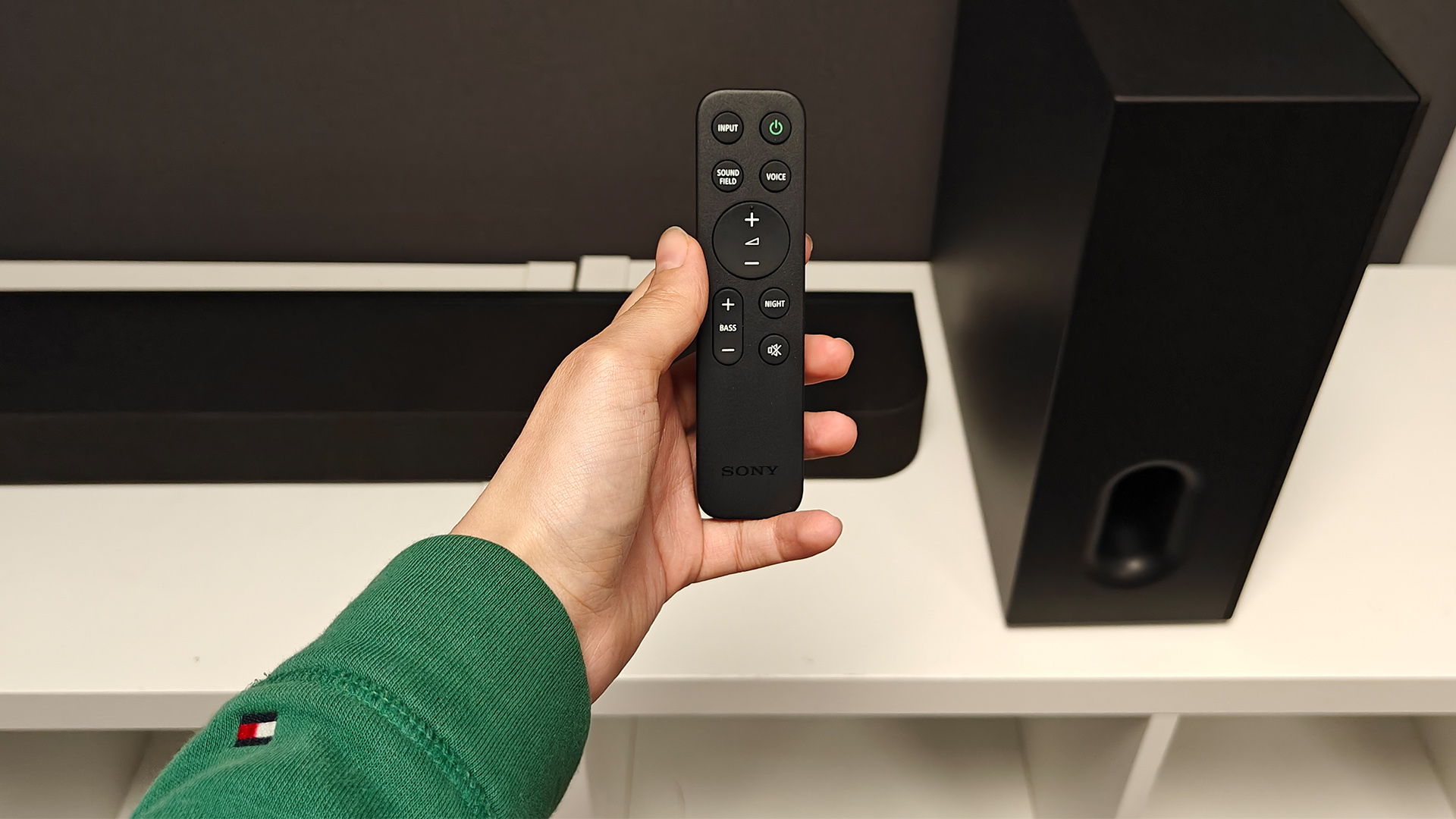 Sony Bravia Theatre Bar 7 + S soundbar package on white shelving unit with remote held in hand above