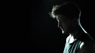 A photograph of Of Mice & Men's Austin Carlile in a very dark room, looking contemplative