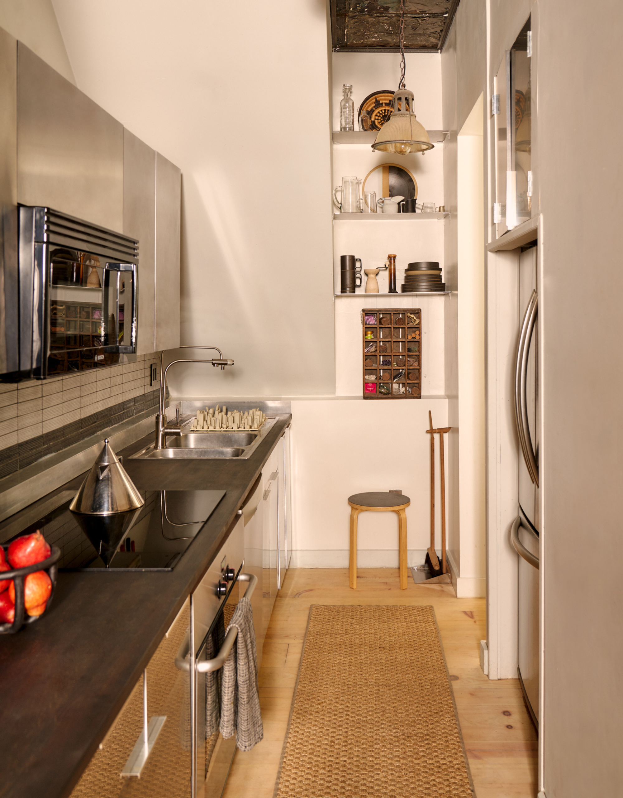 A small NYC loft kitchen with stainless steel cabinets, a wood countertop, a hob, a steel kettle, a storage shelving nook, and a stool