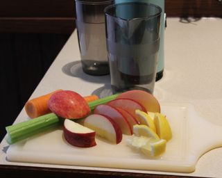 Sliced apples, lemons, celery and carrots on a white plastic cutting board