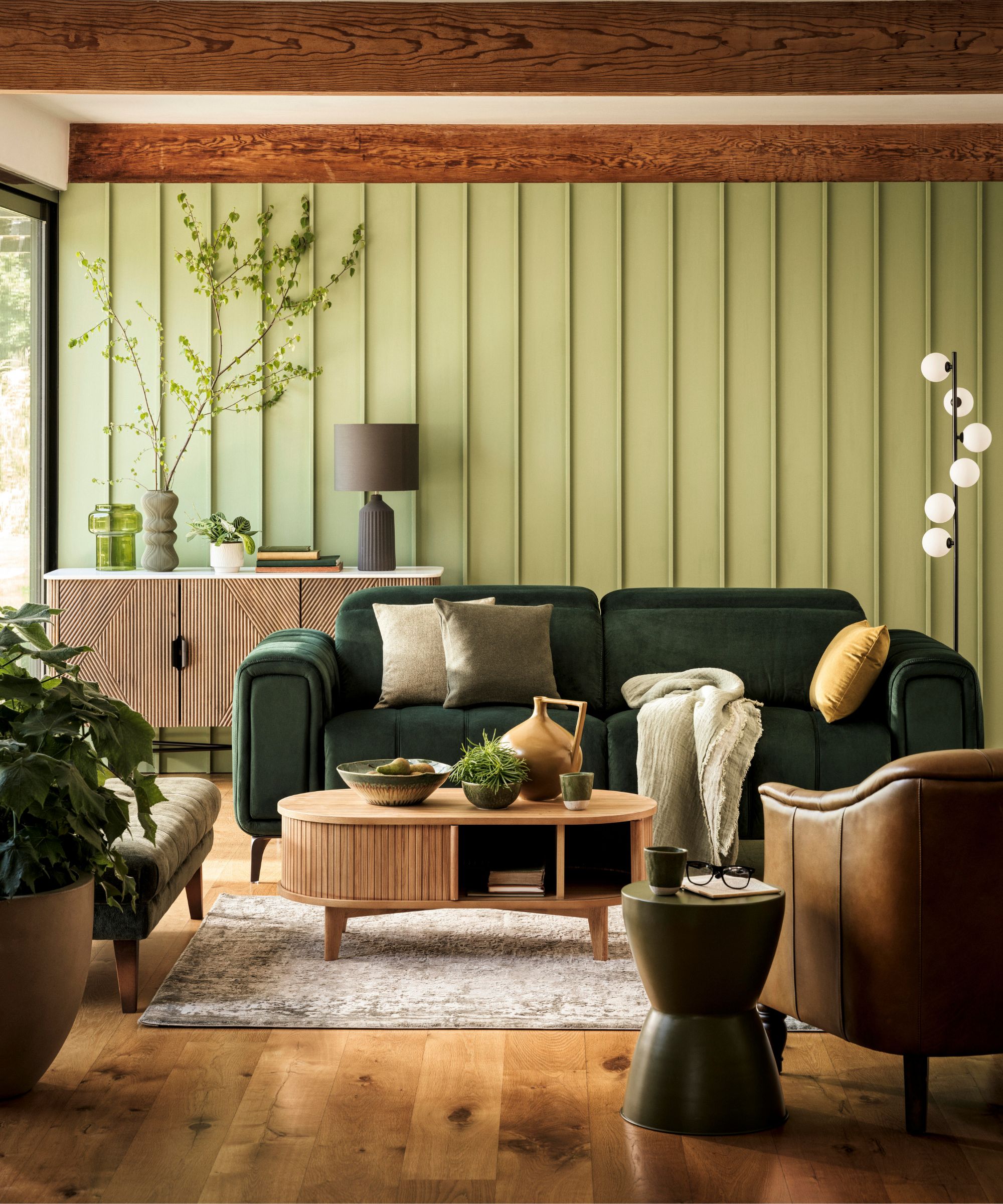 green living room with oak ceiling beams, wooden floor, light green panel walls and a dark green velvet couch