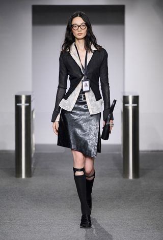 model wearing stylish outfit with socks, including black cardigan over button-down shirt with leather skirt and black knee-high stockings and mules