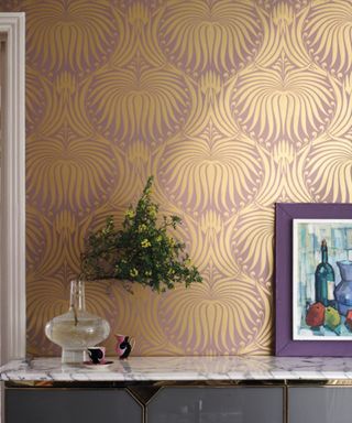 pink and gold patterned wallpaper on wall with marble table and decorative objects