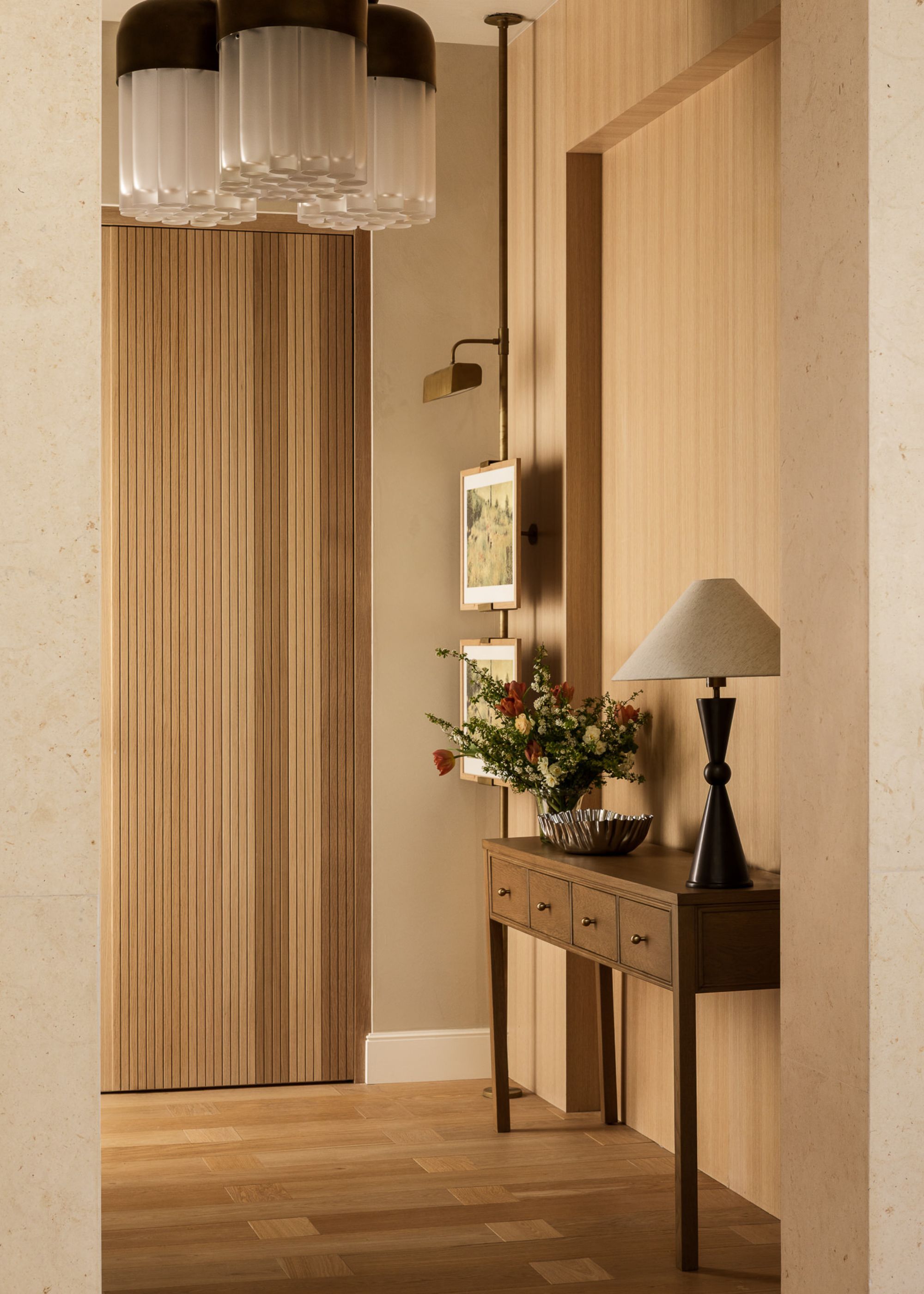 An entryway with wood detailing throughought from the slim paneled door to the panels behind the console table and the wood flooring