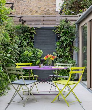 Narrow garden with colourful outdoor furniture and climbing plants growing up its fence