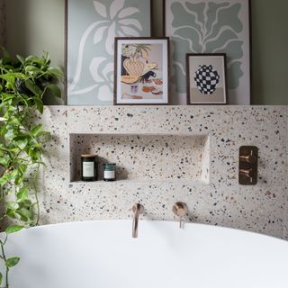 bathroom with large contemporary bath, terrazzo tiles and rose gold brassware, with a shelf featuring framed pictures and a trailing houseplant