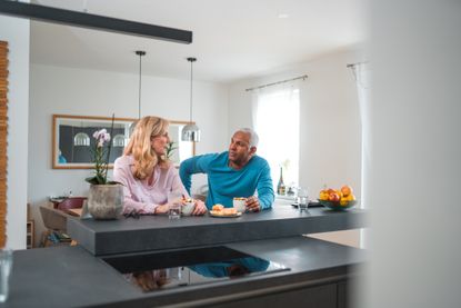 Mature multi-Ethnic couple drinking coffee, bonding and relaxing at home. They are talking and enjoying a peaceful day.
