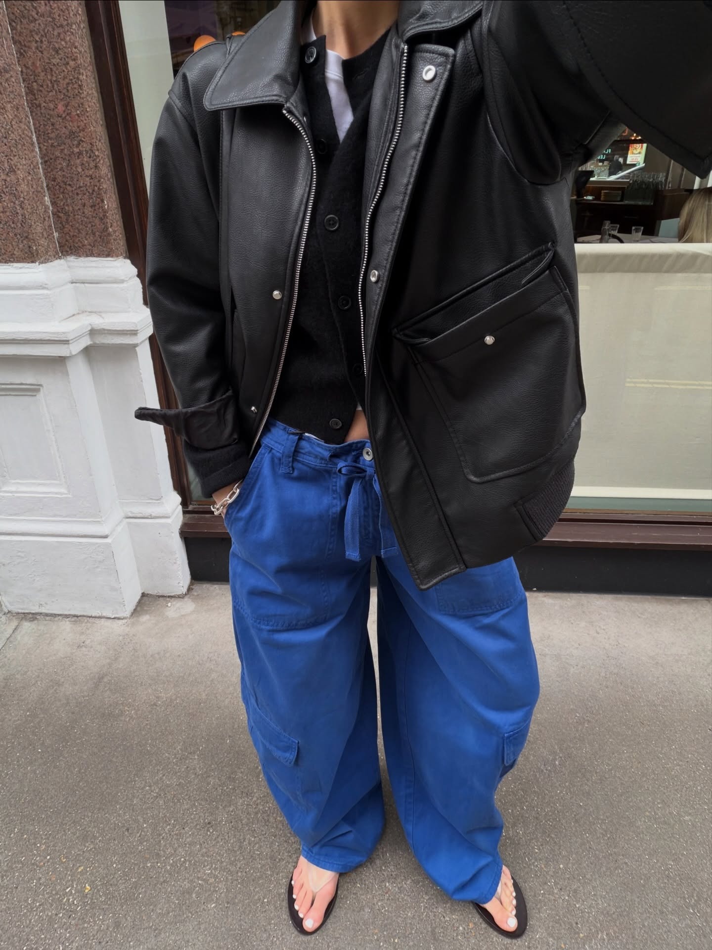 Influencer @thealiceedit wears cobalt blue trousers with a black leather jacket a clear flip flops.