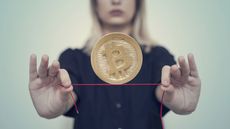 A woman balances a bitcoin on a red tightrope.