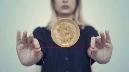 A woman balances a bitcoin on a red tightrope.