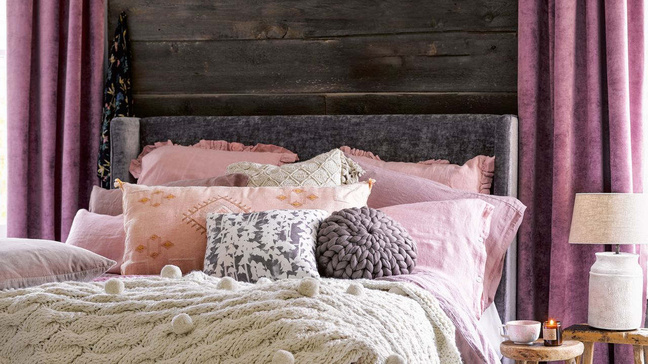 Bed dressed with cosy throws and blankets with dark wood wall panelling and luxe pink curtains