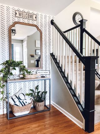 Monochrome entryway with black staircase banister and large mirror, wooden floor and blakc and white wallpaper