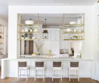 White kitchen with glass and brass hanging shelves above kitchen peninsula island
