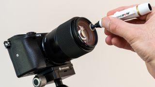 A hand using a Lenspen to clean a camera lens