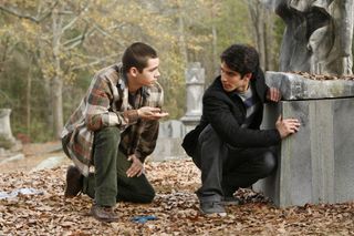 dylan o'brien and tyler posey hiding behind a gravestone in a cemetery in teen wolf