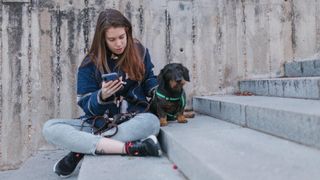 Young woman on smartphone with dachshund looking uninterested