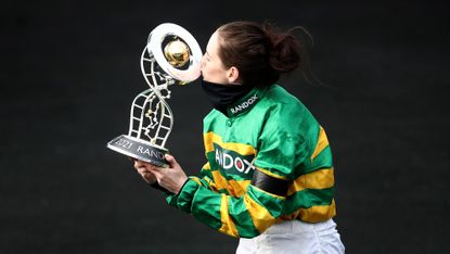 Rachael Blackmore, wearing green and gold silks, kisses the Grand National trophy following her win in 2021 aboard Minella Times.