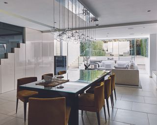A large lower ground kitchen extension with a black dining table with upholstered chairs in front of a living space leading out to a garden through glass doors