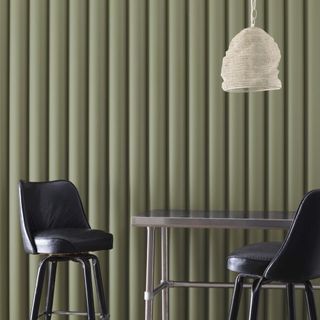 A dark olive green wall and two black barstools