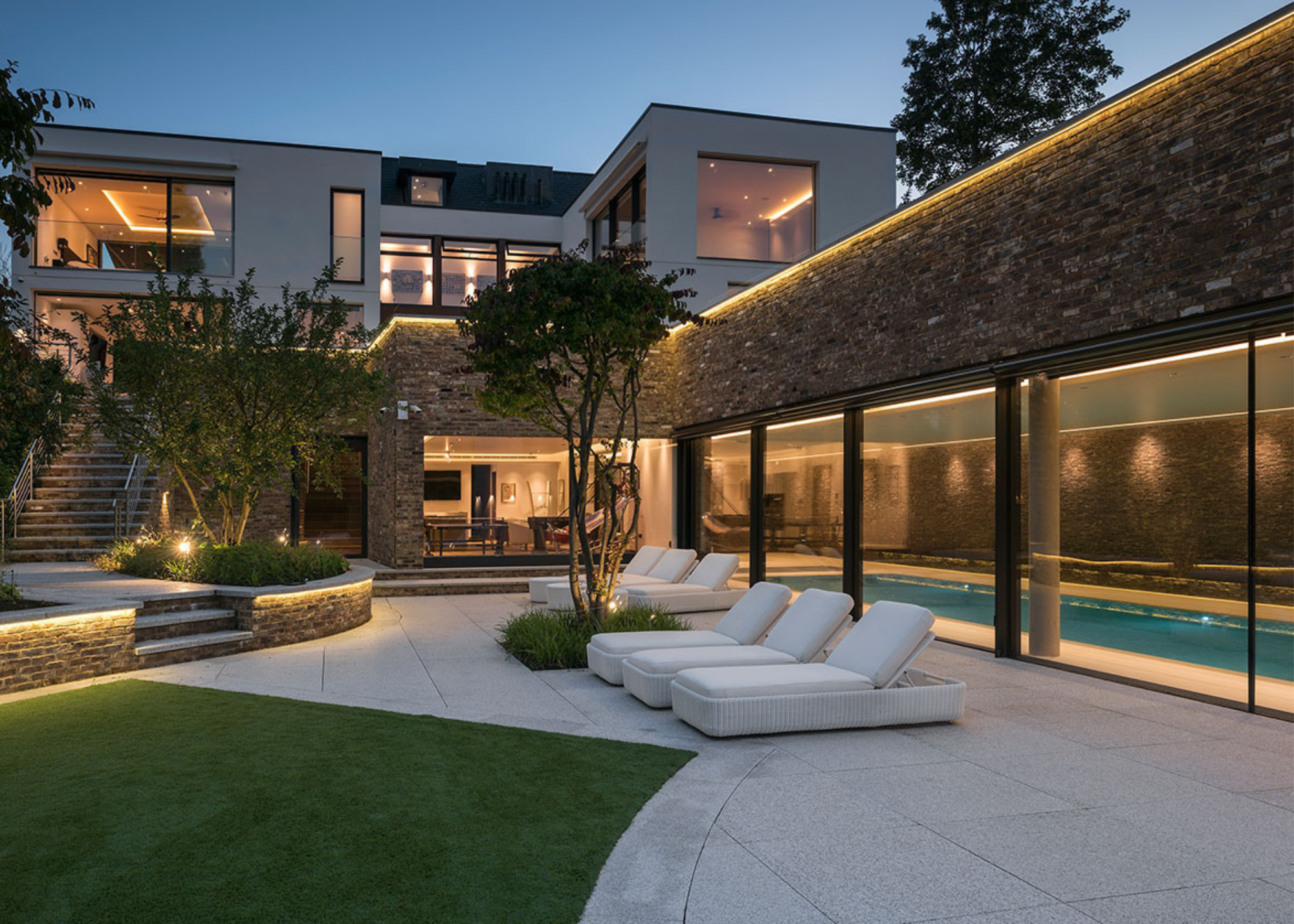 a luxurious garden with led lighting as well as garden furniture and loungers places around with plants and trees