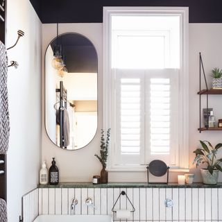 White tiled bathroom with oval mirror and sink with dark vintage wood cabinets