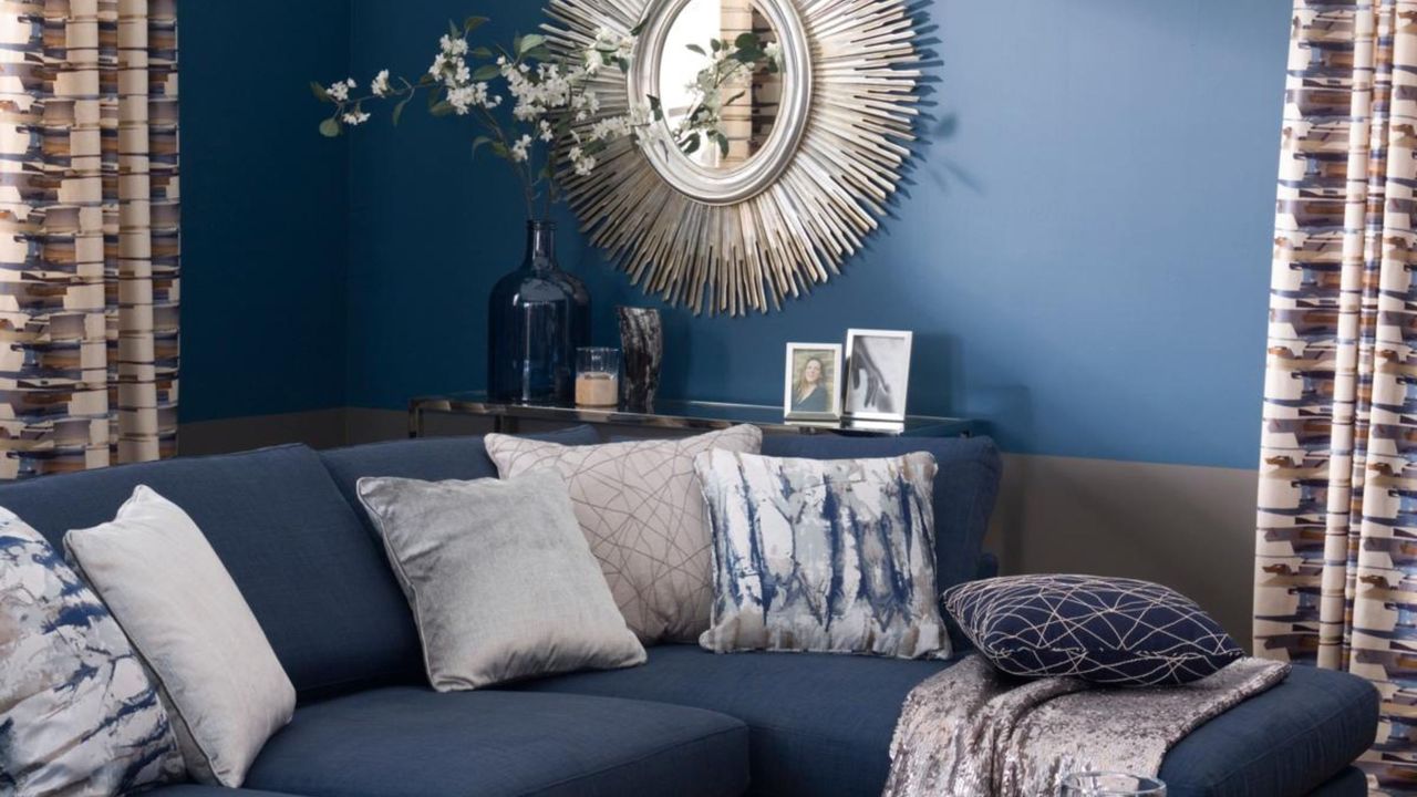 Dark blue living room,matching sofa, grey armchair, wood floorboards, modern lantern chandelier, glass coffee table, modern sunburst mirror.